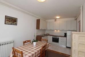 A compact kitchen with white cabinets, a dining table with a checkered tablecloth, and a radiator.