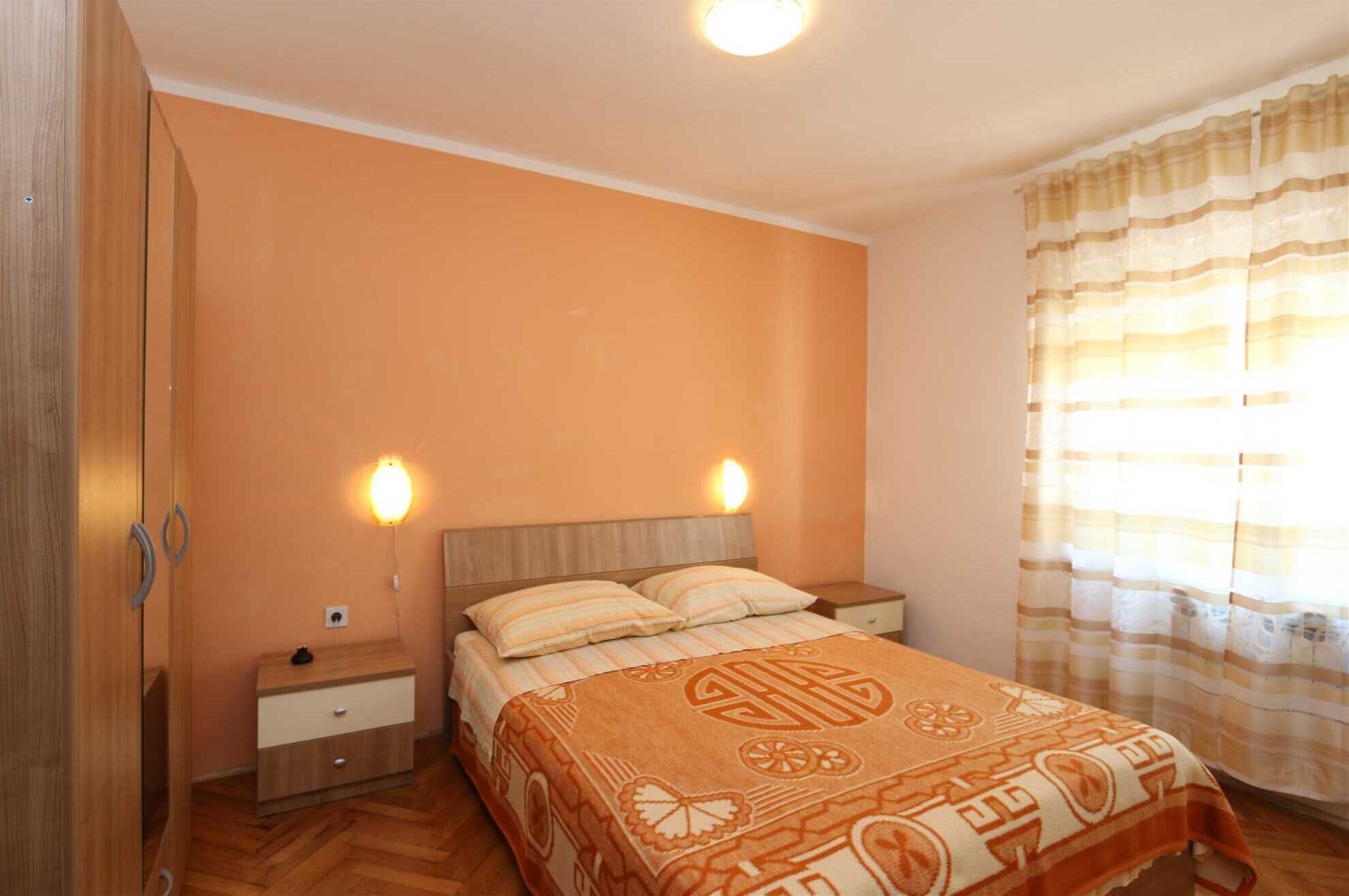 Une chambre à coucher comprenant un lit, des tables de chevet, une armoire en bois et une fenêtre avec des rideaux.