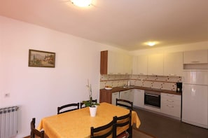 Une cuisine compacte avec des meubles blancs, un four encastré et un coin repas comprenant une table et des chaises.