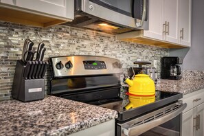 A kitchen with a stainless steel stove, a yellow kettle, and a coffee maker on the counter.
