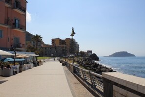 A seaside promenade with outdoor seating, a stone railing, and buildings in the background. - B&B Allerìa (Pozzuoli)