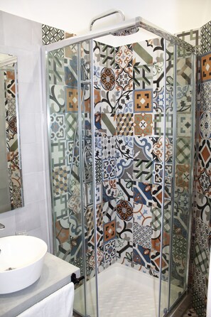 A shower with a glass door and a tiled wall with a geometric pattern. - B&B Allerìa (Pozzuoli)