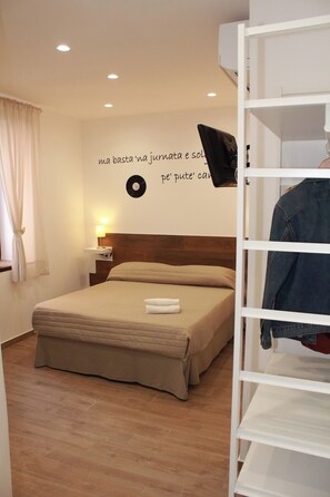 A bedroom with a bed, a nightstand, a wall-mounted TV, and a shelf with a jacket. - B&B Allerìa (Pozzuoli)