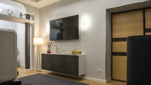 A modern living room with a flat-screen TV mounted on the wall, a dark grey sofa, a wooden cabinet with a fruit bowl, and a grey rug. - Vesù (Naples)