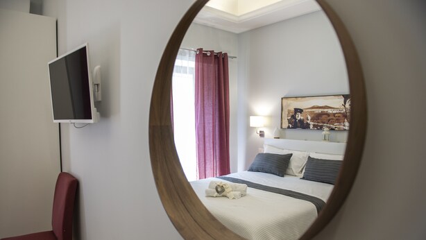 A hotel room with a bed, a TV mounted on the wall, a mirror, and a painting on the wall. - Vesù (Naples)
