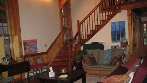 A spacious living room with a wooden staircase, a green sofa, and a coffee table. - Rustic Elegance to Feed Your Soul in the Heart of Pennsylvania (Loganton)