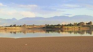 A calm lake with a clear reflection, surrounded by a flat landscape and distant mountains.