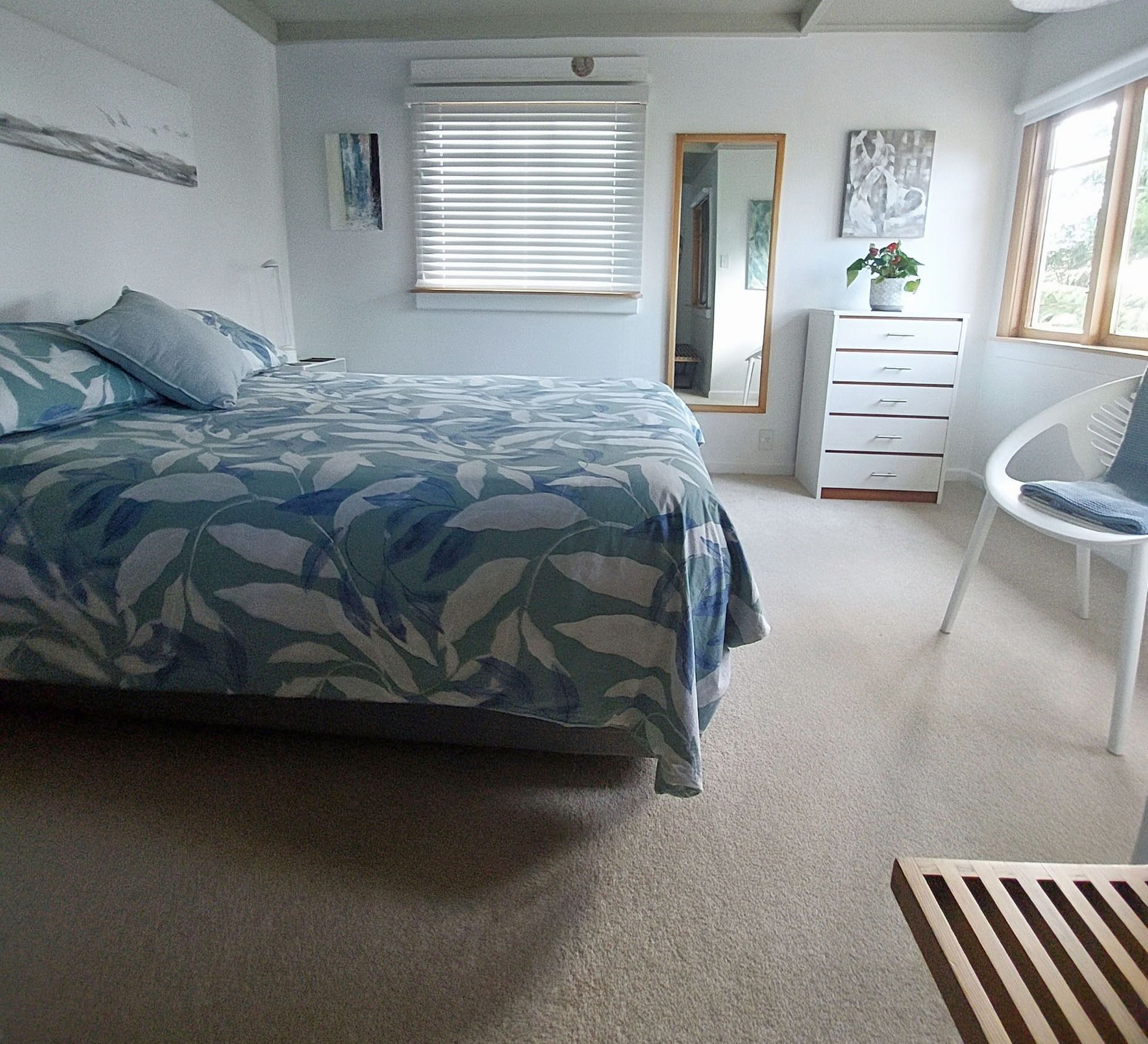 A bedroom with a bed, a dresser, a chair, and a window with blinds.