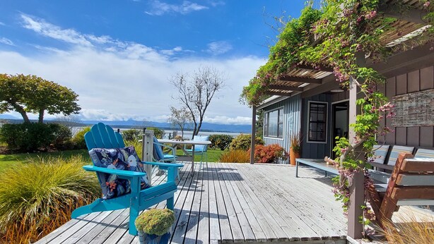 A wooden deck with outdoor seating, a view of the sea, and a building with a covered porch.