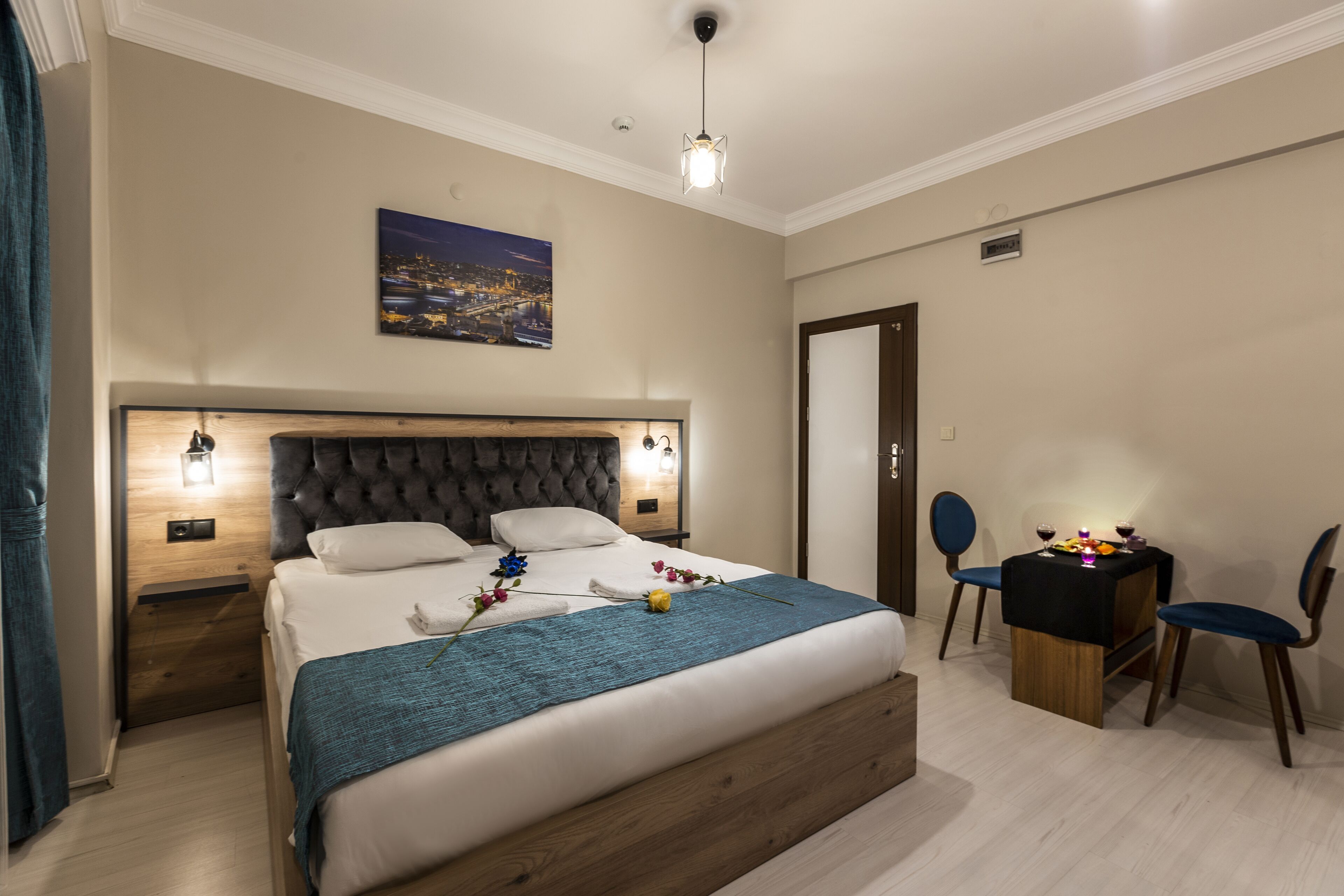 Un dormitorio con una cama grande, mesitas de noche, un escritorio con sillas y un cuadro de un paisaje urbano en la pared.