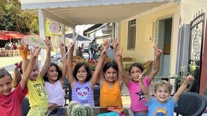 A group of children sitting at an outdoor table with a cactus centerpiece, raising their hands. - Alada Garden Otel (Bozcaada)