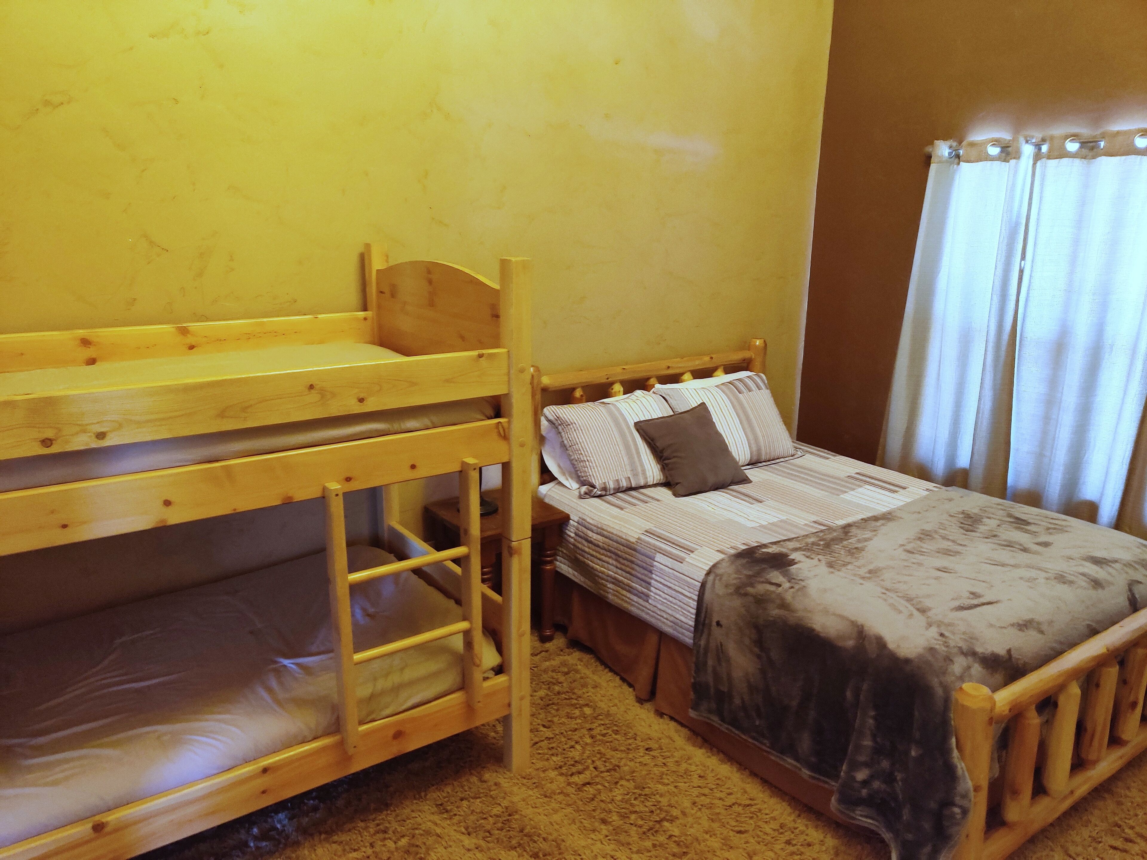 A bunk bed with a lower bunk, a single bed with striped bedding, and a window with curtains.