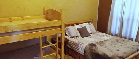 A bunk bed with a lower bunk, a single bed with striped bedding, and a window with curtains.