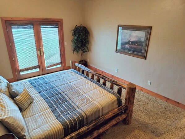 A bedroom with a bed, a window with blinds, a potted plant, and a framed picture on the wall.