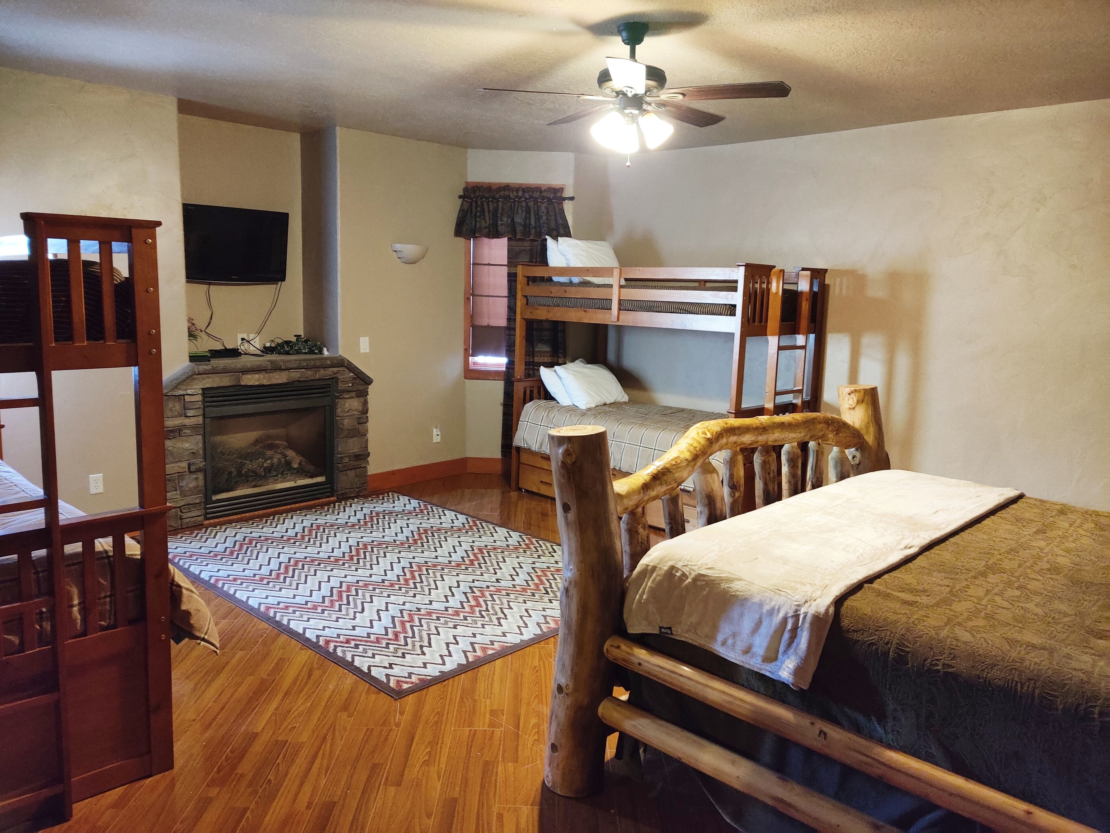 A room with a wooden bunk bed, a fireplace, a ceiling fan, and a patterned rug.