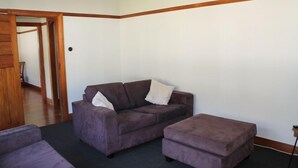 A living room with a dark purple sofa, a matching ottoman, and a wooden door leading to another room. - right in the town centre (Whakatane)
