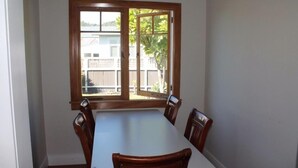 A dining area with a table and four chairs, a window with a view of a fence and trees, and a white wall. - right in the town centre (Whakatane)