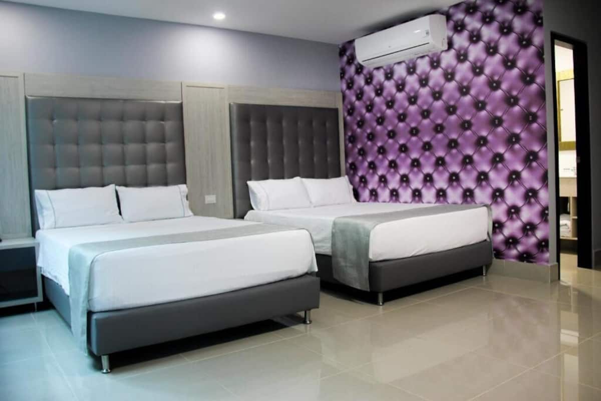 A modern hotel room with two beds, a large padded headboard, and a purple patterned accent wall.