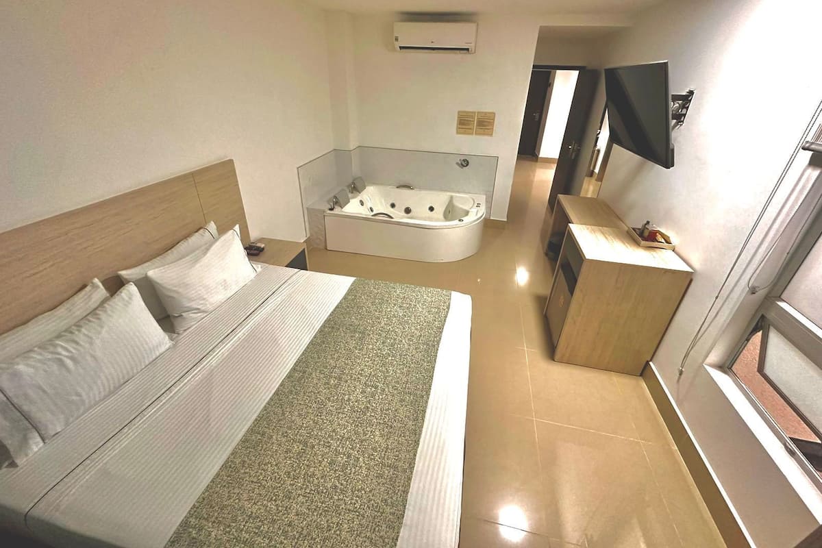 A hotel room with a large bed, a separate bathroom with a bathtub, a small desk, and a TV mounted on the wall.