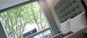 A bedroom with a large window, a tufted headboard, and a bed with white bedding. - Lleras Express (Medellín)
