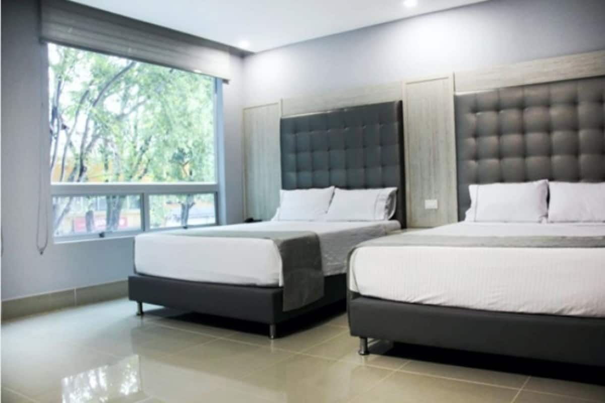 A hotel room with two beds, a large window with a view of trees, and a modern design.