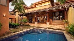 Una propiedad residencial con piscina, un patio cubierto y un edificio de dos pisos con techo de tejas.