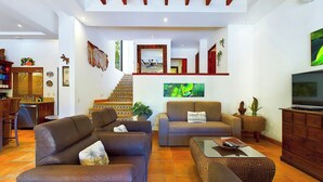 Amplia sala de estar con escalera a un nivel superior, televisor y comedor con cocina.