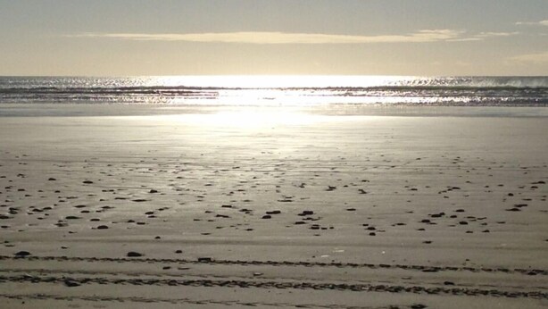 Een strand met een kalme zee en een heldere lucht.