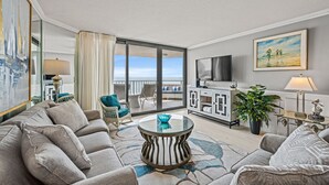 En moderne stue med sofa, sofabord i glas og udsigt til balkon.