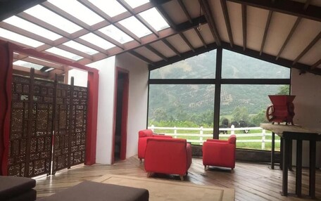 A room with a large window, red chairs, a wooden floor, and a table.