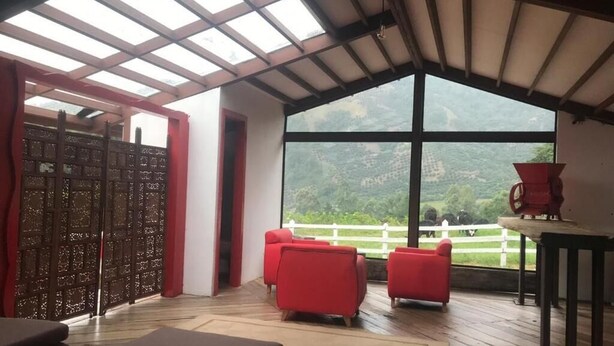 A room with a large window, red chairs, a wooden floor, and a table. - Ecohotel Pinohermoso (Salento)