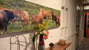 A hallway with a wooden bench, a metal rack, a vase with flowers, and a painting of cows on the wall. - Ecohotel Pinohermoso (Salento)