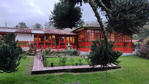 A traditional building with red and white exterior walls, a tiled roof, and a garden with a pathway leading to the entrance. - Ecohotel Pinohermoso (Salento)