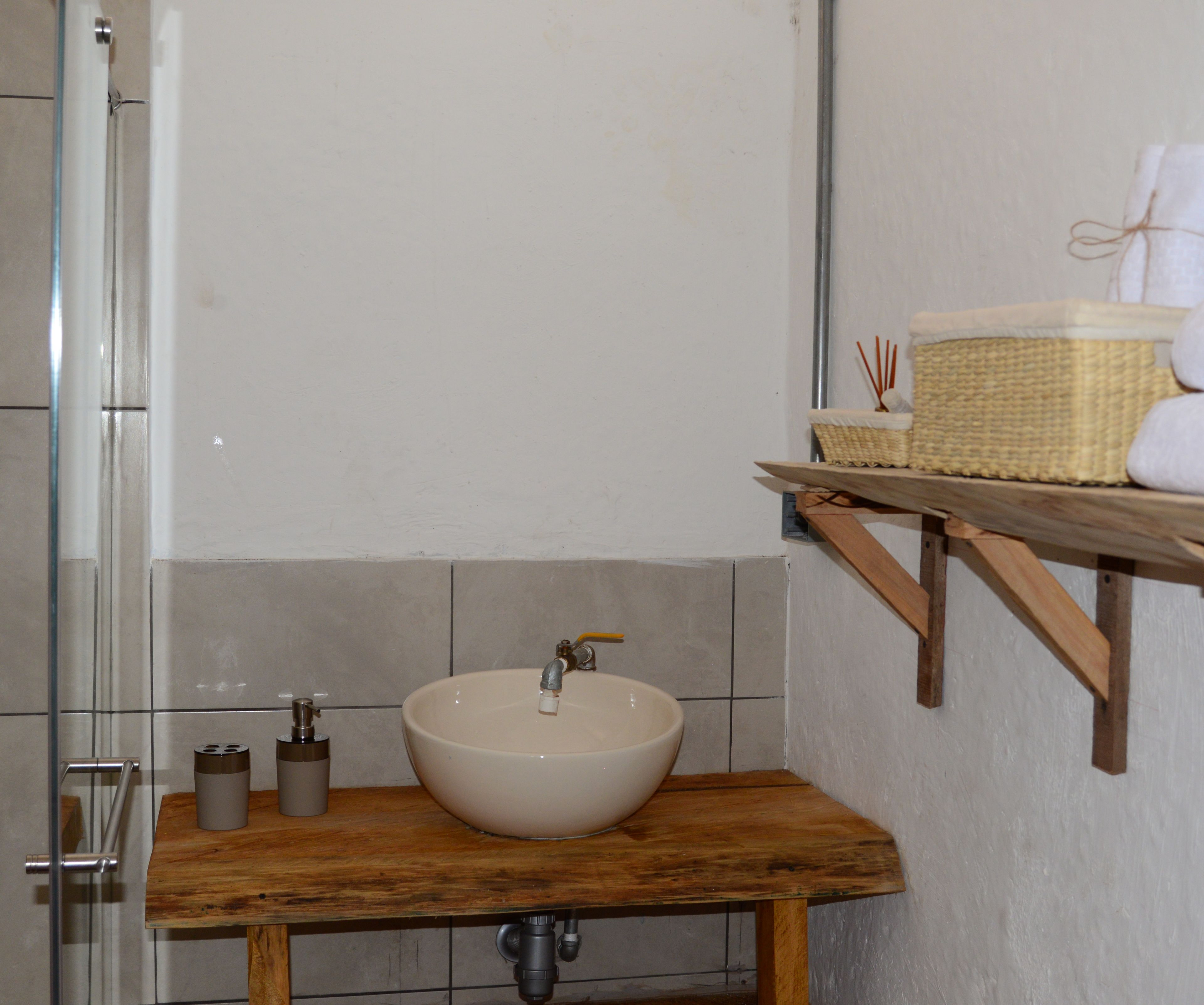 A bathroom with a wooden vanity, a white sink, and a shelf with toiletries.