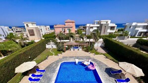 Piscina com espreguiçadeiras e um flutuador decorativo em formato de cisne, rodeada por sebes bem cuidadas e vista para o mar.