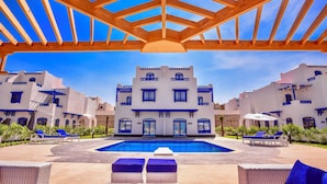 A pool area with a wooden pergola overhead, surrounded by white buildings with blue accents and a clear blue sky. - Sea View Villa with Private Pool (Hurghada)