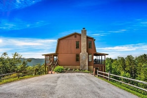A large wooden cabin with a central chimney, a porch, and a view of the surrounding forest.