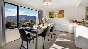 A modern dining area with a view of mountains, a dining table set with chairs, and a kitchen area with a fruit bowl and appliances. - LARGE DISTINCTIVE AND SPACIOUS FAMILY HOME (Queenstown)