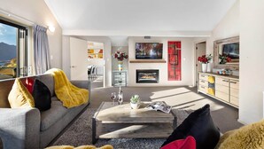 A modern living room with a sofa, coffee table, and fireplace. There is a TV mounted on the wall and a window with a view of mountains. - LARGE DISTINCTIVE AND SPACIOUS FAMILY HOME (Queenstown)
