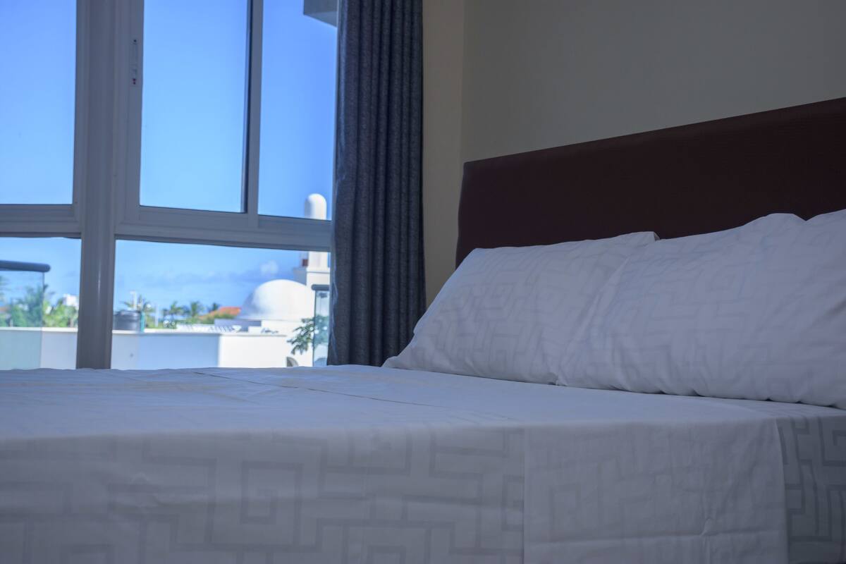 A hotel room with a large window, a neatly made bed, and a view of the cityscape.