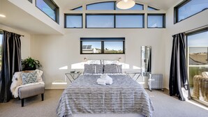 Une chambre spacieuse avec un grand lit, une vue sur l’extérieur grâce à de nombreuses fenêtres, un radiateur et une plante en pot.