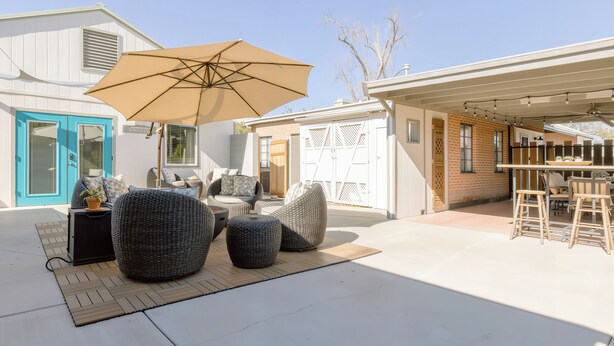 A patio area with outdoor seating, including round and square chairs, a large umbrella, and a bar area with stools. - Visit Sports and Culture Venues from an Artful Garden Studio in Central Phoenix (Phoenix)