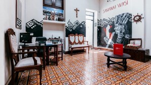 A room with a patterned floor, a desk with a computer, a chair, a bench, and a wall with a mural. - Samanai Wasi Hostel  (Lima)
