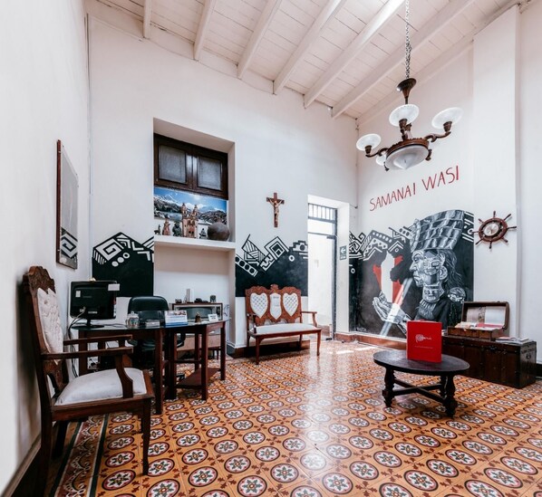 A room with a patterned floor, a desk with a computer, a chair, a bench, and a wall with a mural.