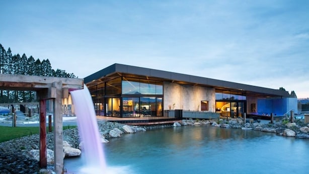A modern building with large glass windows, a waterfall feature, and a view of a river. - Somers holiday cottage (Mt Somers)