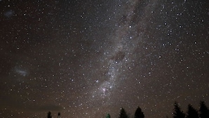 A night sky filled with stars, a house with a visible roof and chimney, and a few trees in the foreground. - Somers holiday cottage (Mt Somers)