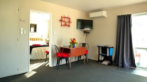 A hotel room with a bed, a desk with two chairs, a TV, a bookshelf, and a window with curtains. - Somers holiday cottage (Mt Somers)