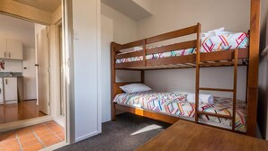 A bunk bed room with a kitchen in the background. - Greenview Retreat - Central, Heating, Sleeps 6 (Rotorua)