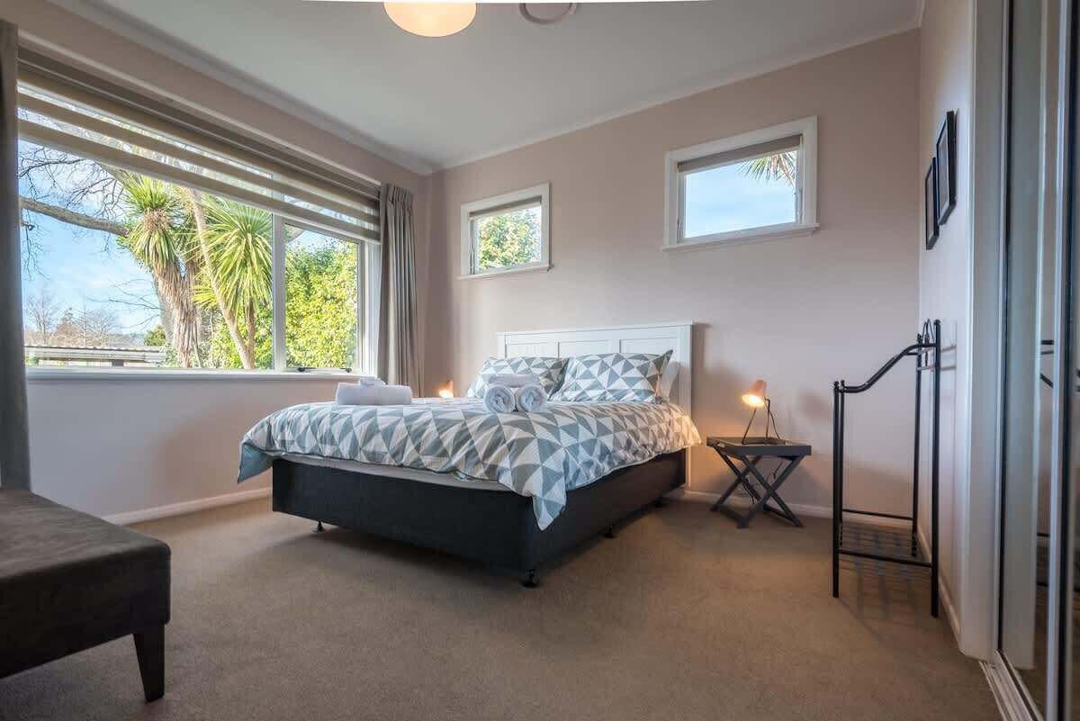 A bedroom with a bed, two windows, a bedside table, and a chair.