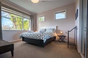 Ein Schlafzimmer mit Bett, zwei Fenstern, einem Nachttisch und einem Sessel.
